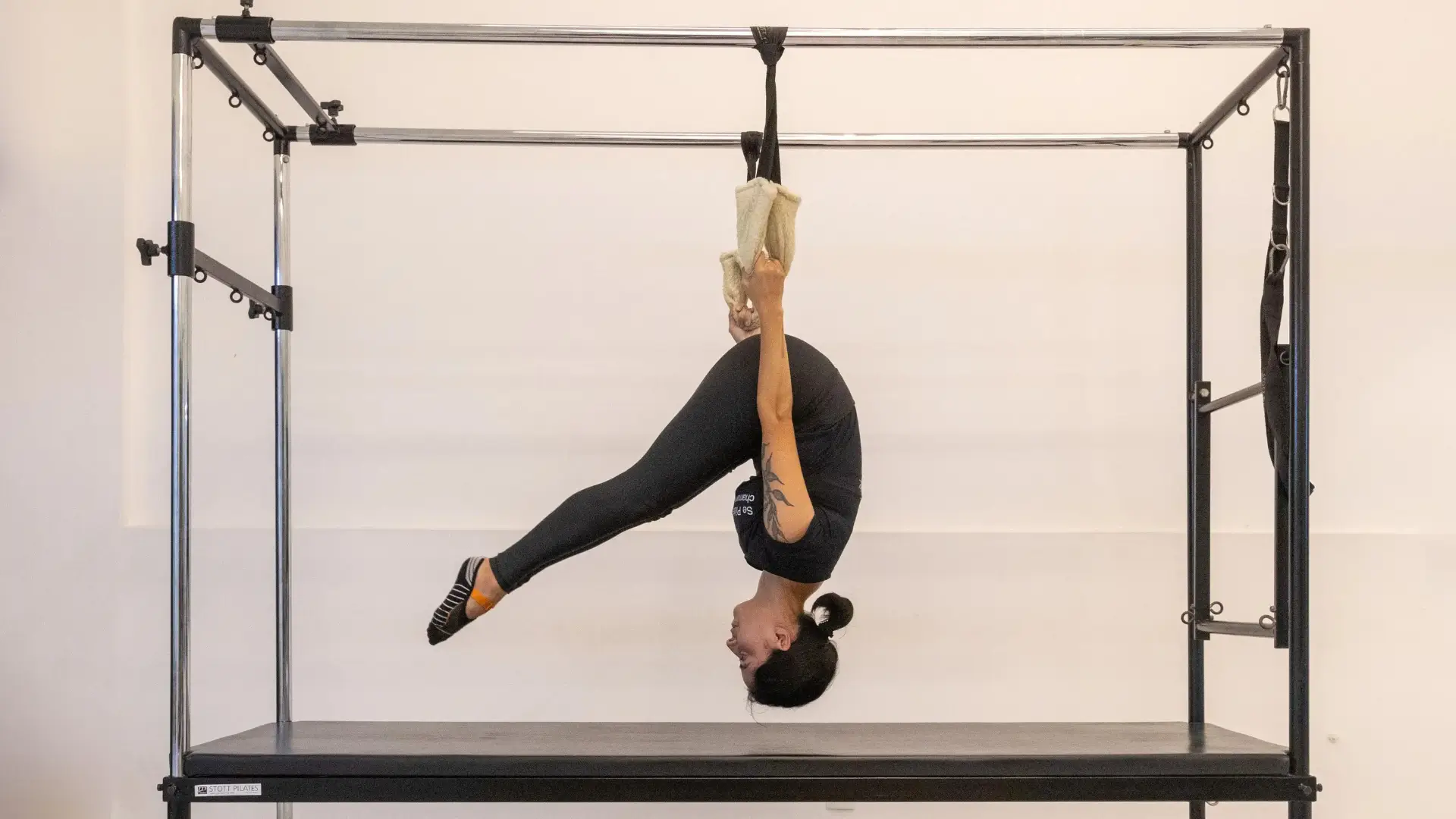Aluna em exercício suspenso no Cadillac, equipamento clássico de Pilates